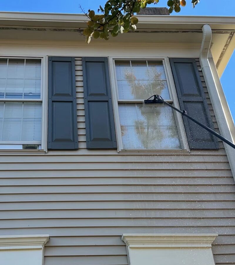 Extension pole reaching second-story siding and windows on a house with tan siding and dark shutters