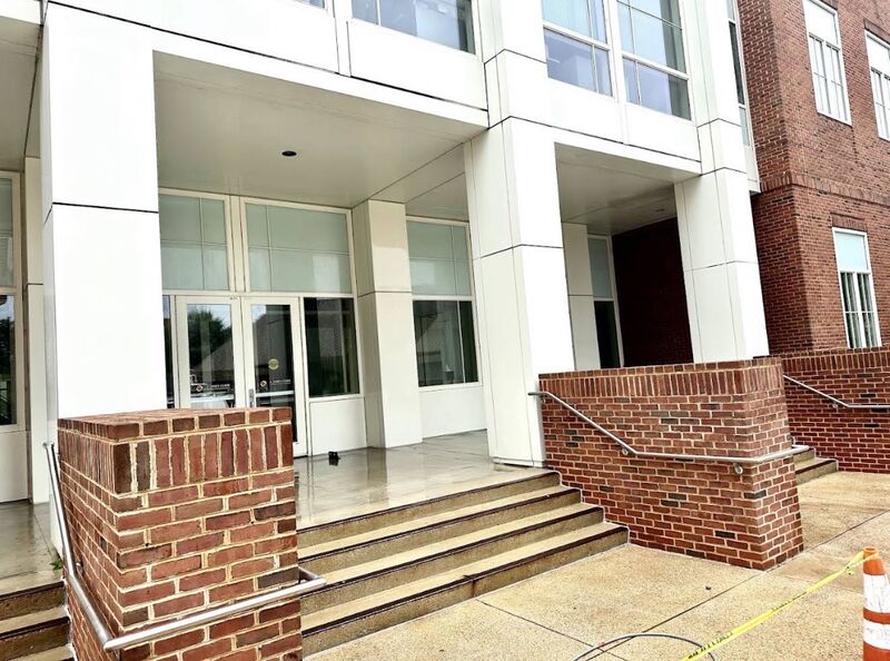 Brick and concrete entrance of an institutional building after cleaning, with caution tape marking the work area
