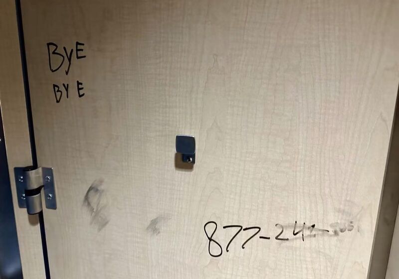 Light wood restroom stall door with black marker writing and scuff marks