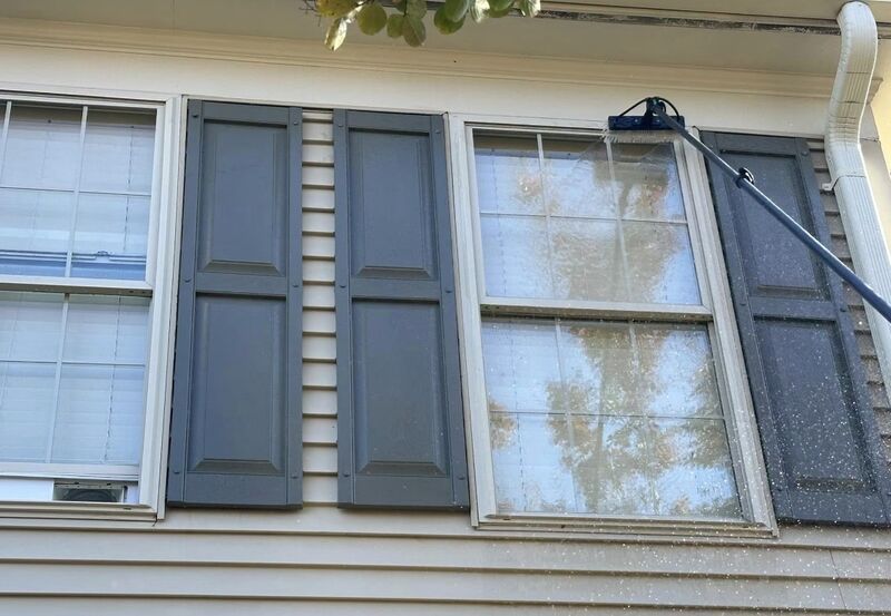 Second-story windows with dark shutters being soft washed from an extension pole